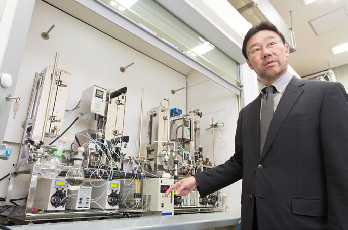 フロー合成の装置を説明する小林教授。"机の上の製薬工場"の実用化は間近だ。
